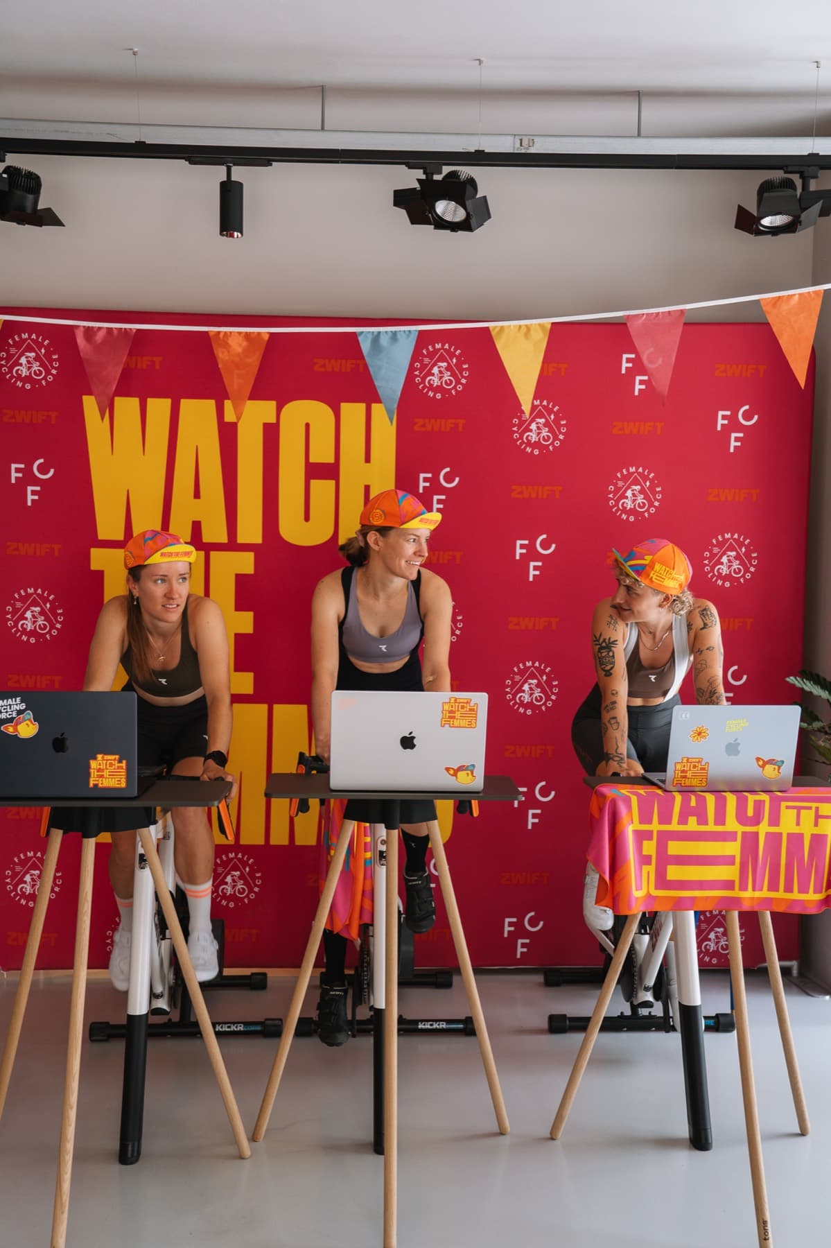 Drei FCF-Mitglieder arbeiten an Laptops an Stehpulten vor der Watch-the-Femmes-Wand im Clubhouse