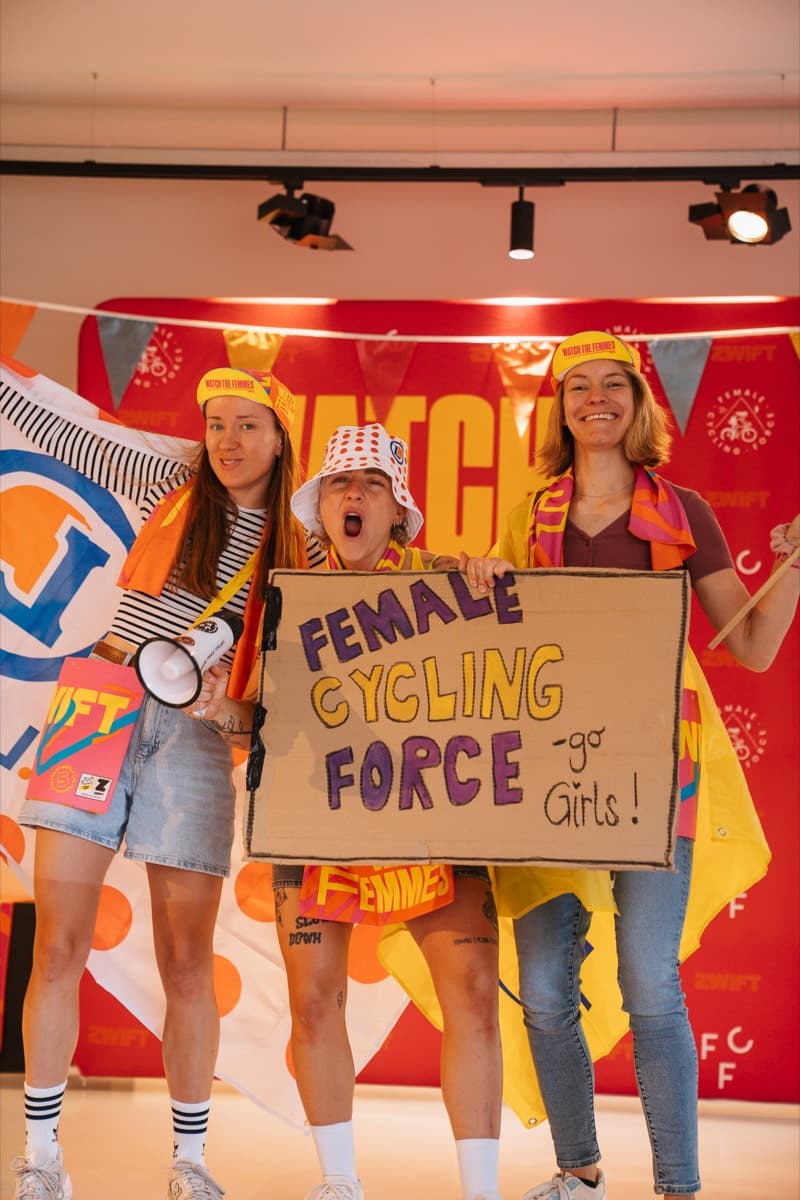 FCF-Mitglieder mit Megafon und Schild vor der Watch-the-Femmes-Wand